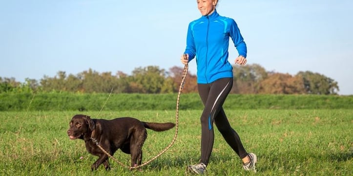 A woman running with her dog in a field