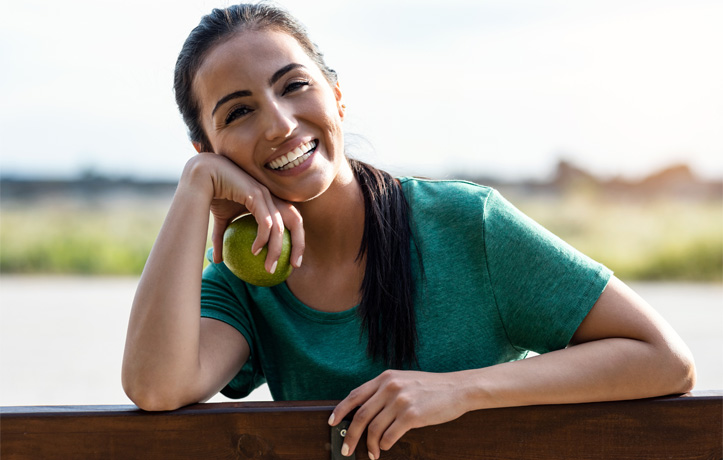 A woman on a fence with an apple in her hand