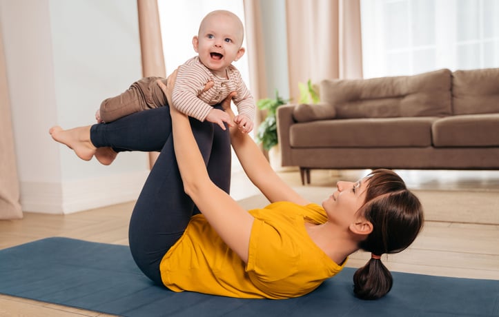 mom laying on a yoga matt with her baby on her legs